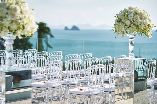 White flower and roses bouquet decoration with the transparent vase on the mirror box with transparent ghost chairs line up, panoramic ocean view