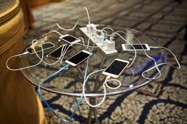 Group of smartphones charging on the glass table with sharing the same AC plug clipart