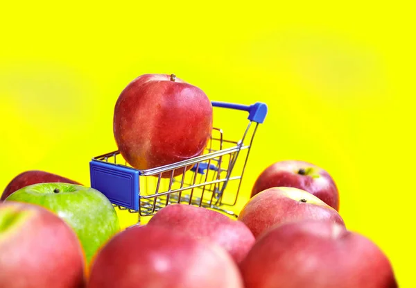 Close-up, Selective focus red apple on mini shopping cart with bright yellow mustard background and some red and green apples in forground. with copy space or text space, Supermarket concept.
