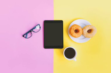 Modern ev ofis işyeri, bir fincan kahve, çörek, gözlükleri ve kopya alanı ile sarı pastel pembe tablete