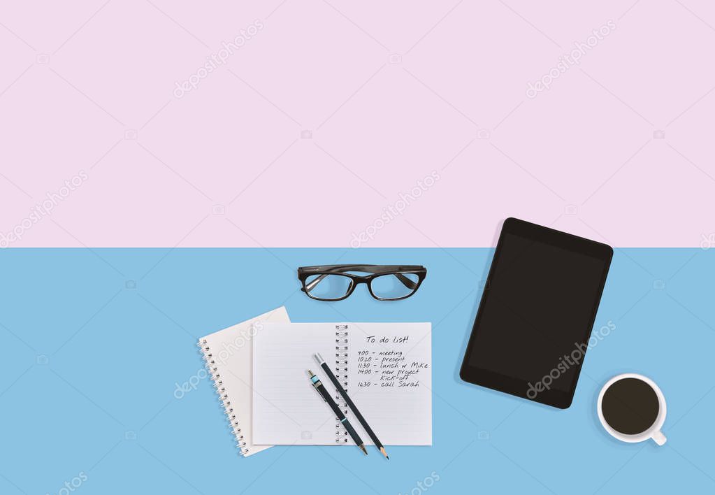 Personal business man workplace desktop in pastel color background with notebook with notes, eyeglasses, tablet, pen, pencils and a cup of black coffee with copy space. Business person workplace concept.