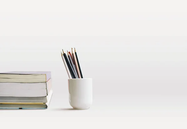 Kurşun kalem, kalem ve kitap kopya alanı ile beyaz masaya istifleme beyaz fincan. Yan görünümü. Öğrenme, eğitim, eğlence, yaşam kavramı.