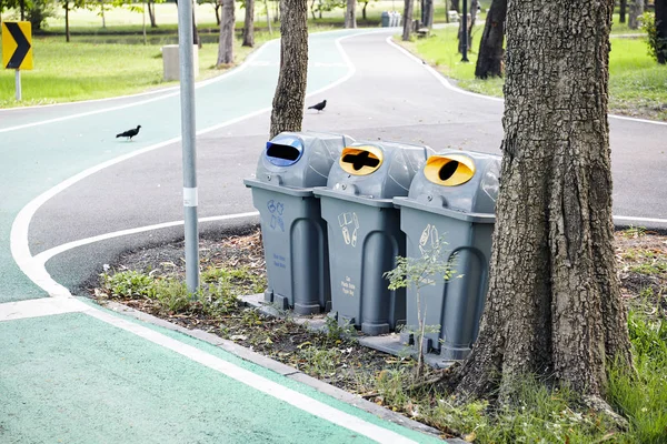 Recycling container of gray trash can dustbins beside the bike lane in the park