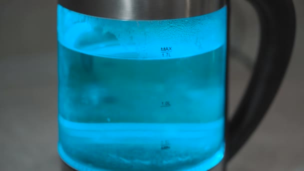Bouilloire électrique en verre avec des lumières bout. L'eau bleue bout dans une bouilloire gros plan. La bouilloire s'éteint. Vidéo 4k 
