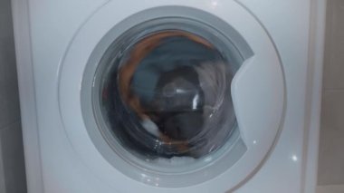 Womam hafifçe renkli Çamaşırhane çamaşır makinesi koyuyor. Genç bir kız çamaşır makinesi ayak Kapıyı kapatır. Çamaşır makinesi davul elbiseleri yıkar. 4k video.