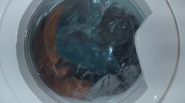 Womam hafifçe renkli Çamaşırhane çamaşır makinesi koyuyor. Genç bir kız çamaşır makinesi ayak Kapıyı kapatır. Çamaşır makinesi davul elbiseleri yıkar. 4k video.