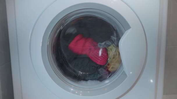 Womam sta delicatamente mettendo il bucato colorato in lavatrice. Una ragazza chiude la porta del piede della lavatrice. Il tamburo della lavatrice lava i vestiti. 4k video . — Video Stock