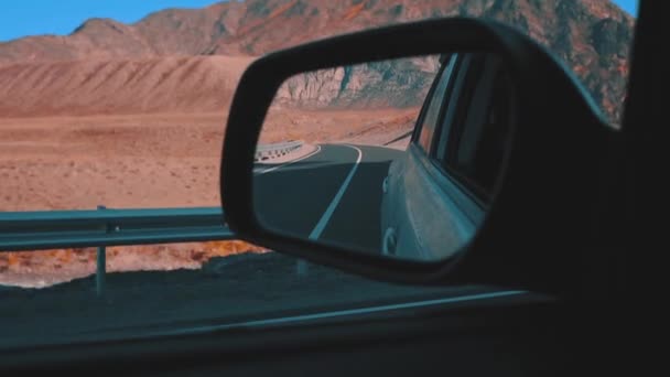 Rearview mirror gray car. View from moving car during trip in desert road, back road reflected in car mirror. Mountains and desert in the background. — Stock Video