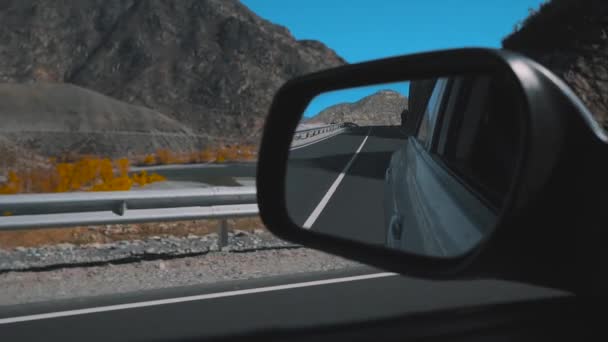 Retrovisor gris coche. Vista desde el coche en movimiento durante el viaje en carretera del desierto, camino de vuelta reflejado en el espejo del coche. Montañas y desierto en el fondo . — Vídeos de Stock
