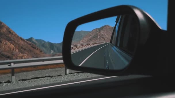 Rearview mirror gray car. View from moving car during trip in desert road, back road reflected in car mirror. Mountains and desert in the background. — Stock Video