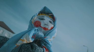 Mavi gökyüzüne karşı saman kuklası. Bebek karnavalda yakılacak. Kamera yavaş hareket içinde paçaları etrafında hareket.