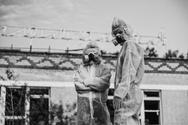 Two scientists put on a respirator and a radiation protective suit. Stern look into the camera from the abandoned territory. Coronavirus in a pandemic, COVID-19. Care about ecology in black and white photo mystical horror movie. clipart