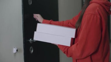 Kırmızı üniformalı bir pizza cıvıltıcısı genç bir kıza iki kutu getirmiş. Nakliye için nakit transferini kapatın. Pizzanın parasını öde. Modern mal arzı. Close. 4k video.