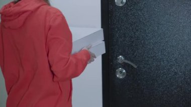 Kırmızı üniformalı bir pizza cıvıltıcısı genç bir kıza iki kutu getirmiş. Nakliye için nakit transferini kapatın. Pizzanın parasını öde. Modern mal arzı. Close. 4k video.
