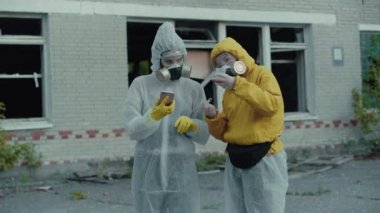 İki bilimadamı bir solunum cihazı takıp araştırma yaptılar. Çevre tehlikede. Coronavirus salgını, COVID-19. Radyasyon yüzünden koruyucu giysili iki kız. Veriyi telefona girin.