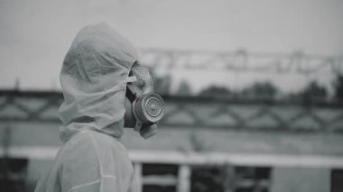 Bilim adamı bir solunum cihazı ve koruyucu bir bornoz giydi. Coronavirus salgını, COVID-19. Kız - bir öğrenci terkedilmiş bir binanın arka planındaki ekolojiyi kontrol ediyor. Solunum cihazına yakın çekim.