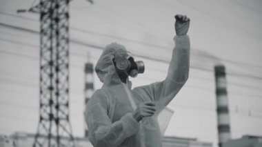 Bilim adamı bir solunum cihazı ve koruyucu bir bornoz giydi. Bir öğrenci fabrikanın arka planındaki ekolojiyi kontrol ediyor. Coronavirus salgını, COVID-19. Zararlı kimyasallar havayı kirletir. Novosibirsk