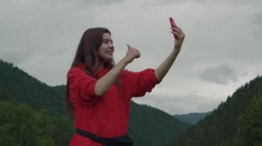Kırmızı kazak konuşma videochat cep telefonu arkadaş bağlantı Dağları genç kız. Internet her yerde. Dağlarda mevcut mükemmel iletişim.