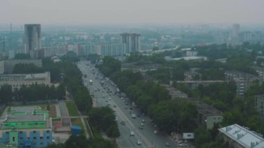Şehir sis inde, arabalar yol boyunca gidiyor. Otoyolun çatısından manzara. Kaldırım boyunca daha yeşil ağaçlar yetişir. Rusya'da pürüzsüz yol.