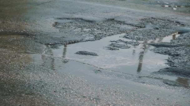 水たまりで満たされた道路上の大きな穴 車の車輪が汚れのある穴に落ちる ロシアの悪い道 春のクローズアップで雨や雪の後のほこりっぽい泥道 — ストック動画