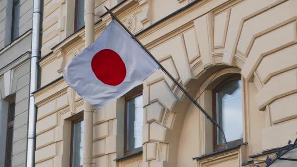 La bandera japonesa se está desarrollando en el contexto de un antiguo edificio arquitectónico amarillo. Consulado de Japón en Rusia . — Vídeo de stock