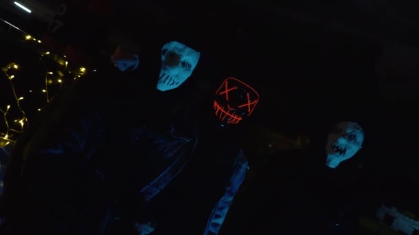 Les gens avec des masques de purge lumineux tiennent une batte de baseball et katana. Assassins la nuit dans le parking sur fond de voiture avec une guirlande. — Video