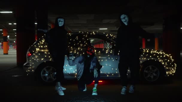 People with luminous purge masks are holding a baseball bat and katana. Killer at night in the parking lot against the backdrop of a car with a garland. — Stock Video