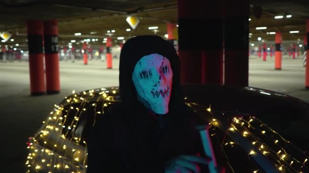 주차장에서 무서운 마스크를 쓰고 있는 남자. 범인은 숙청 을 준비하고 있어요. 할로윈을 위해 철조망으로 감싼 야구 방망이. 위험 한 차는 화랑으로 장식되어 있다. — 비디오