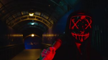 Neon maskeli adam duman üflüyor. Kalın yeşil ve kırmızı duman. Korkunç Cadılar Bayramı Katil Arınma kostümü.