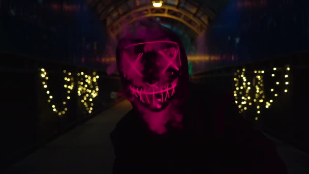 Muž v neonové masce fouká kouř. Silně zelený a růžový kouř. Strašidelný halloween čistit vrah kostým. — Stock video