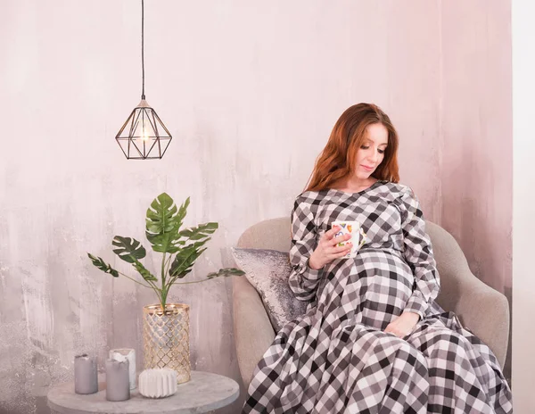 The red-haired pregnant woman sits in a chair. Pot-belly of the pregnant woman