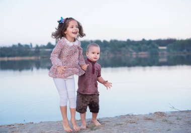 Küçük kardeşim ve kız kardeşi nehir kenarında iyi eğlenceler. Mutlu çocukluk. Aile yürür ve mutluluğunu atlar