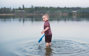 Çocuk giysileri göle duruyor. Bir oyuncak çocukların beach için dinlenmek güzel çocuk elinde