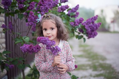 Lila bush yakınındaki ilkbaharda kıvırcık saçlı kız. Güzel Bebek portresi