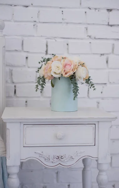 Beautiful flowers in a box of soft blue color and stand on a carved wooden pedestal. the interior in the room girls