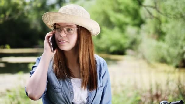 Jasne brunetka dziewczyna w kapeluszu rozmawia przez telefon, na zewnątrz — Wideo stockowe