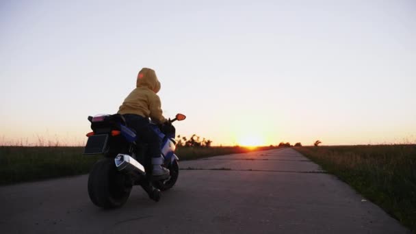 Трехлетний мальчик на игрушечном мотоцикле по дороге — стоковое видео