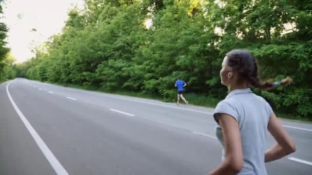 Läufer und Läuferin laufen auf offener Straße im Grünen — Stockvideo