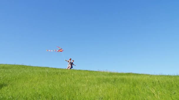 I bambini corrono giù per la collina verde con un aquilone volante — Video Stock