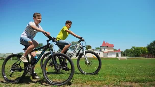 Dois amigos em passeio de bicicleta no campo de grama verde juntos — Vídeo de Stock