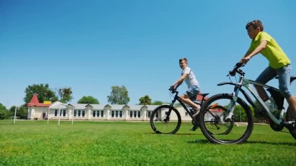 Два друга катаются на велосипеде по зеленой траве вместе — стоковое видео