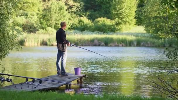 Un joven está pescando en un estanque — Vídeo de stock