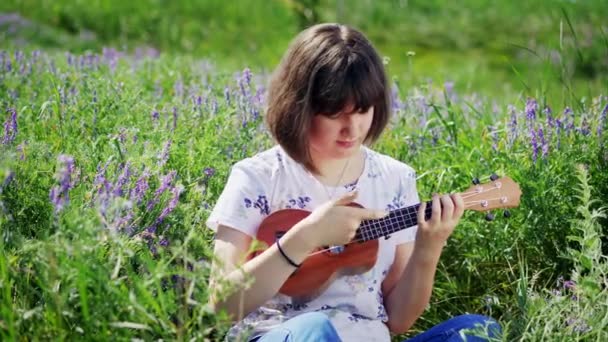 Młoda piękna dziewczyna gra na gitarze ukulele — Wideo stockowe