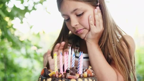 Šťastná dívka sedí u stolu v zahradě a obdivuje slavnostní dort — Stock video