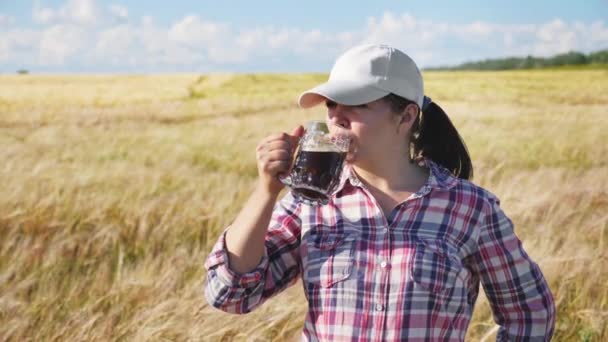 Vrouwelijke boer drankje donker bier in gerst veld — Stockvideo