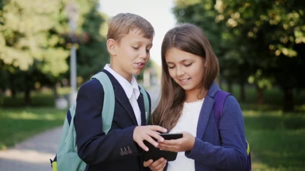 Duas crianças em idade escolar usam um tablet ao ar livre — Vídeo de Stock