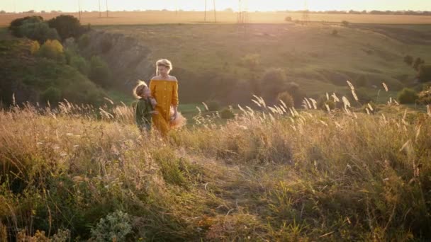 ママと小さな娘夕日丘の上に一緒に歩きます 子供と家族 相互理解で良好な関係 背面図 — ストック動画