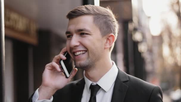 Young man speaking and smiling on a mobile at the street — Stock Video