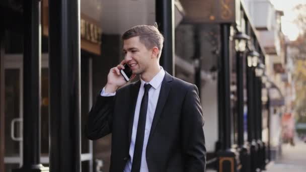 Jonge man spreken en glimlachend op een mobiele telefoon op de straat — Stockvideo