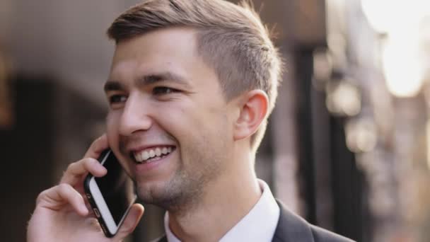 Young man speaking and smiling on a mobile at the street — Stock Video